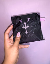 Load image into Gallery viewer, Black pouch with light pink cross design held by a hand against a light purple background